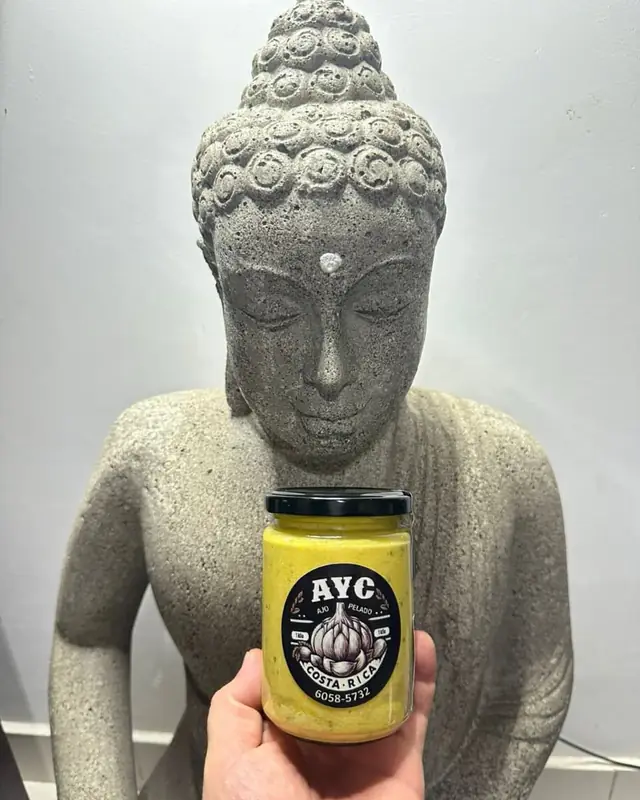 Frasco de mantequilla de ajo con perejil con etiqueta AYC, sostenido frente a una estatua