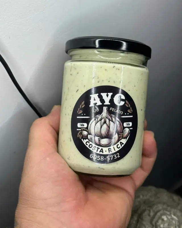 Frasco de pasta de ajo con tomillo con etiqueta AYC, en la mano