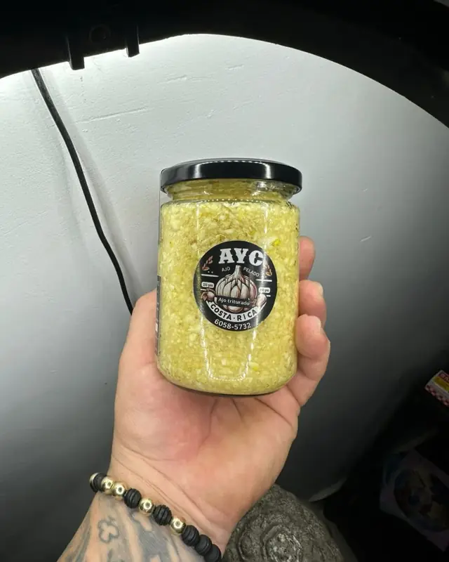 Frasco de ajo triturado puro con etiqueta AYC, en la mano