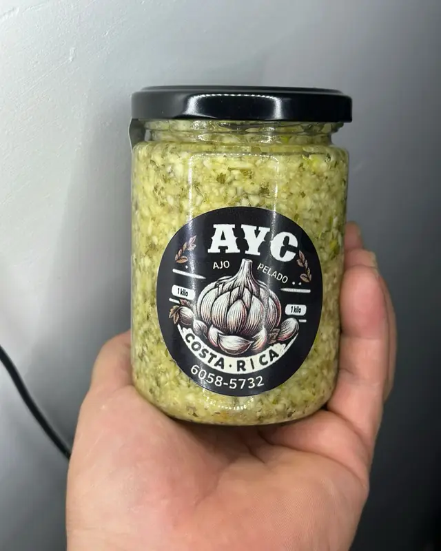 Frasco de ajo triturado con yerbas con etiqueta AYC, en la mano