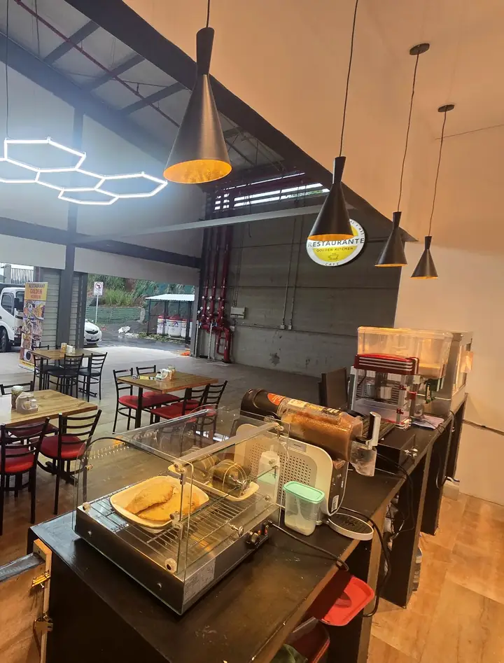 El local de Golden Kitchen por dentro: techo alto, lámparas colgantes, su rótulo redondo en la pared, mesas con sillas rojas y el mostrador