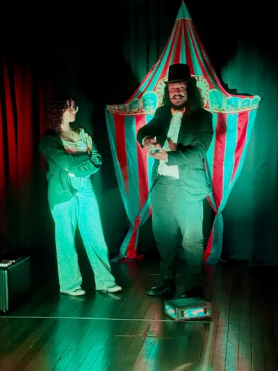 Maestro de ceremonias de sombrero de copa frente a una carpa de circo iluminada en verde