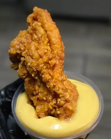 Un dedo de pollo mojado en salsa, sostenido con guante negro