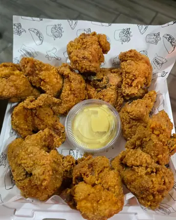 Piezas de pollo frito con un vasito de salsa en la bandeja de Pollo Elí