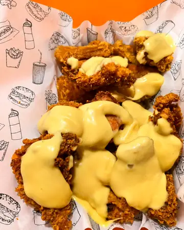 Pollo frito bañado en queso derretido sobre el papel de bandeja de Pollo Elí
