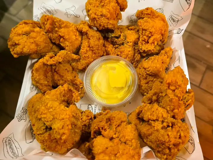 Trocitos de pollo frito con su vasito de salsa, sobre el papel de bandeja de Pollo Elí